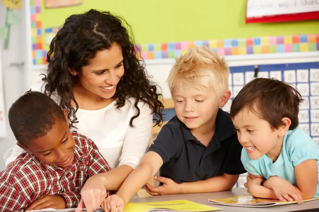 Montessori educator smiling while three preschool children explore a book together at Beehouse Montessori Daycare