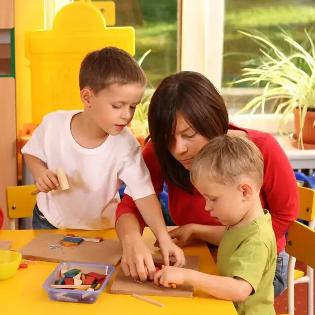 Educator guiding two young boys through a hands-on woodworking activity in a bright classroom